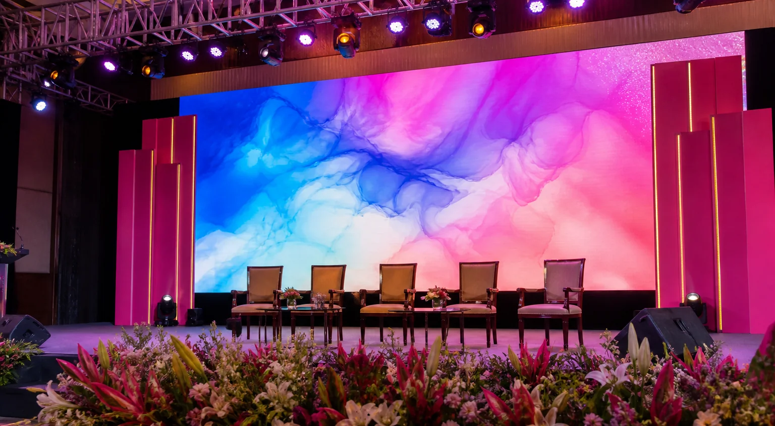 A stage with lighting truss, LED wall and floral foreground in an event hall